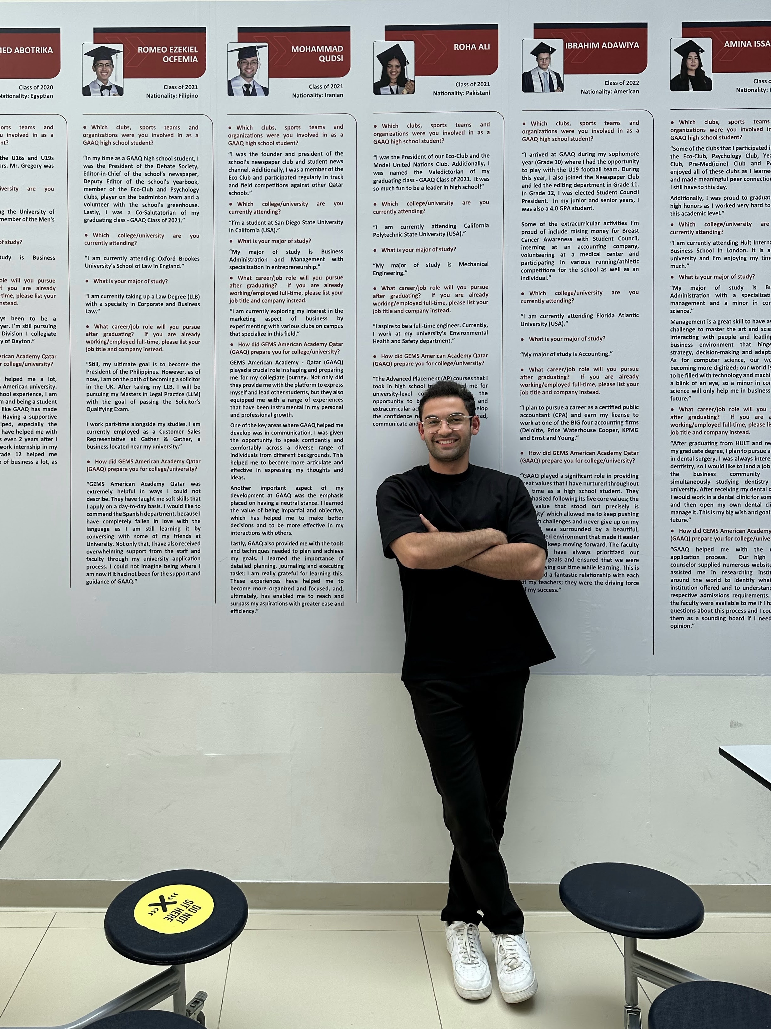 Qudsi standing beside his featured student spotlight on the school wall