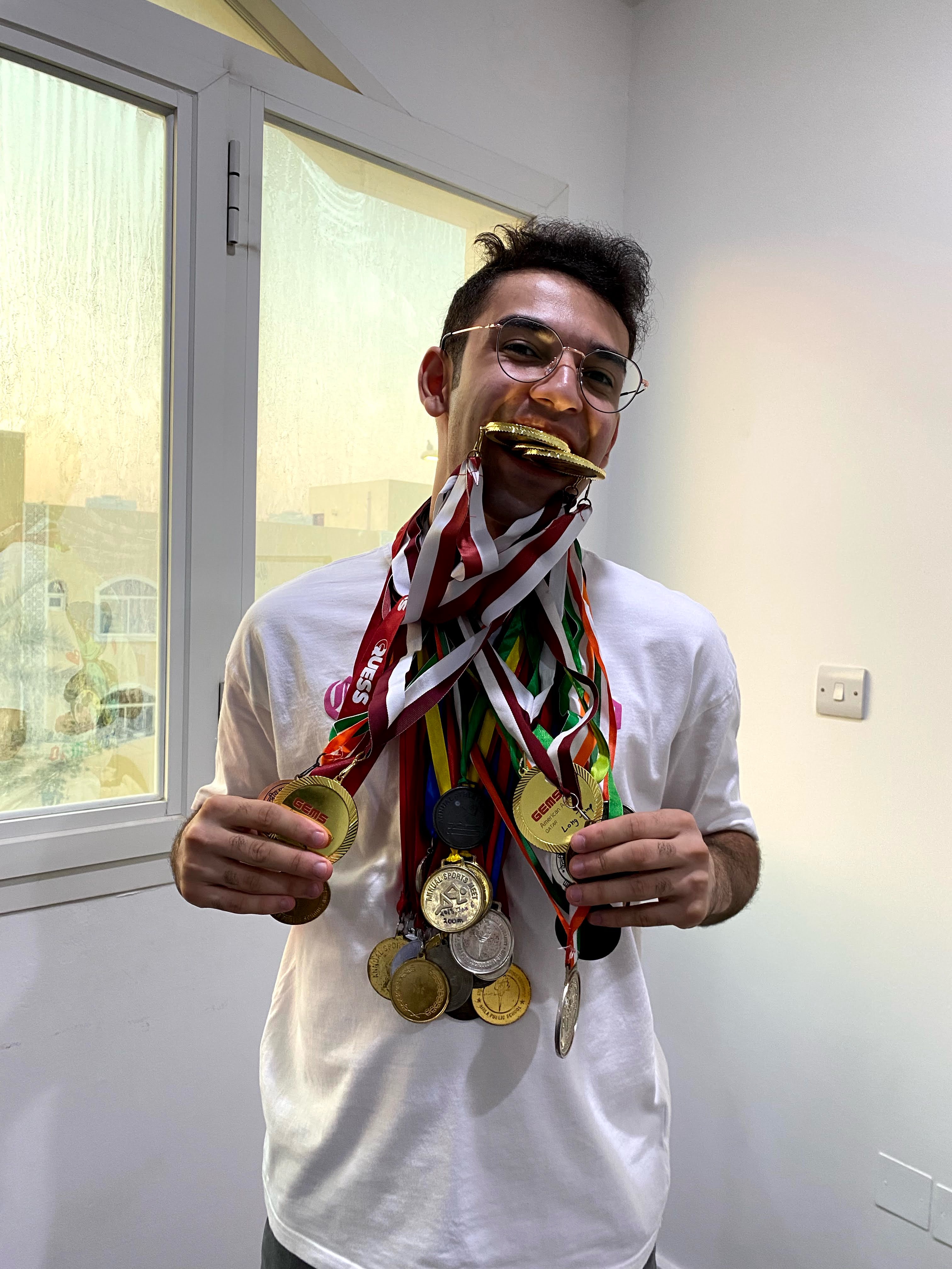 Qudsi biting a gold medal, draped in dozens of track and field medals